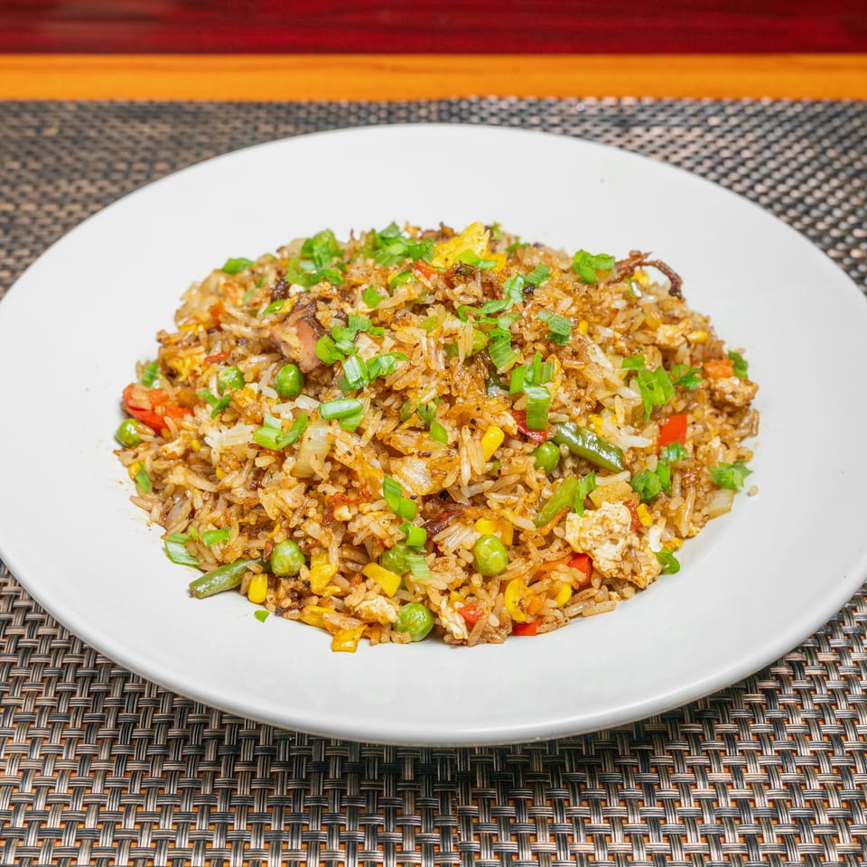 Plate of colorful fried rice with mixed vegetables, egg, and green onions on a white dish.