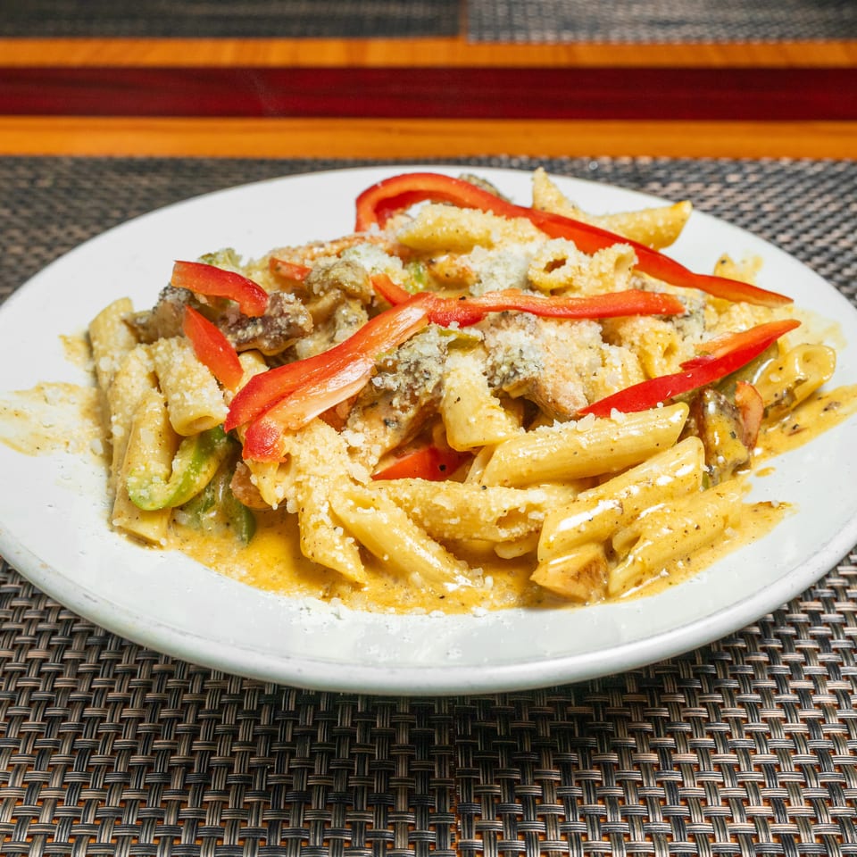Creamy penne pasta with chicken, mushrooms, vegetables, red pepper strips, and breadcrumbs served on a white plate.